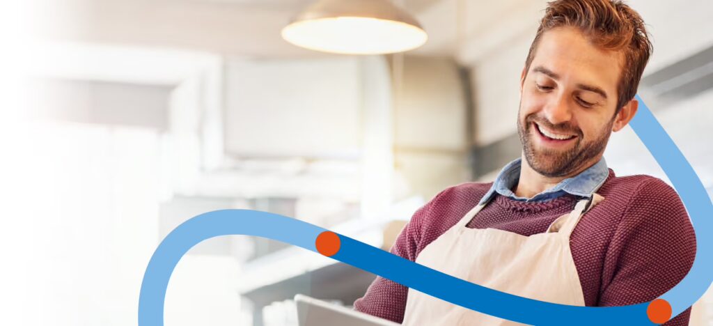 Smiling man in an apron looking at a tablet, with decorative curved lines in the foreground